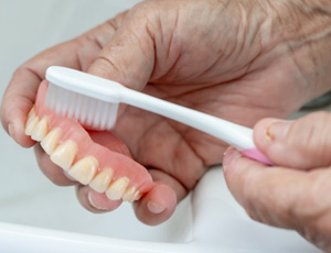 Close up of patient brushing their denture over the sink