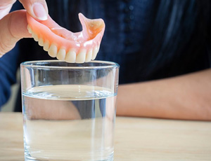 Close up of patient dropping their denture into a cleaning solution