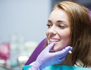 Patient smiling while dentist examines their smile with purple glove