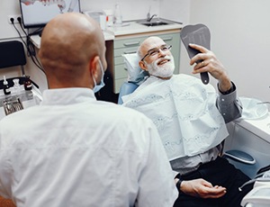 man with dental implants in Harrisburg admiring his smile in the mirror 