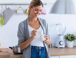 woman standing in her kitchen and eating yogurt 