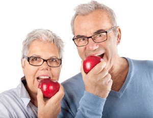 elderly man and woman biting into red apples
