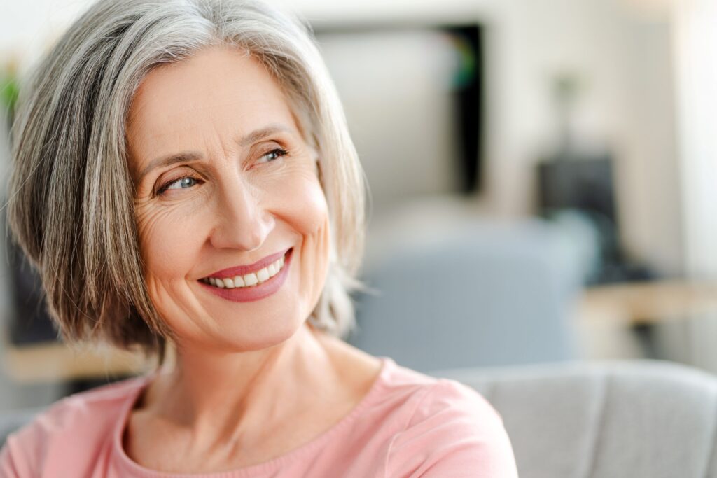 Woman with short gray hair in pink shirt smiling looking off to the side